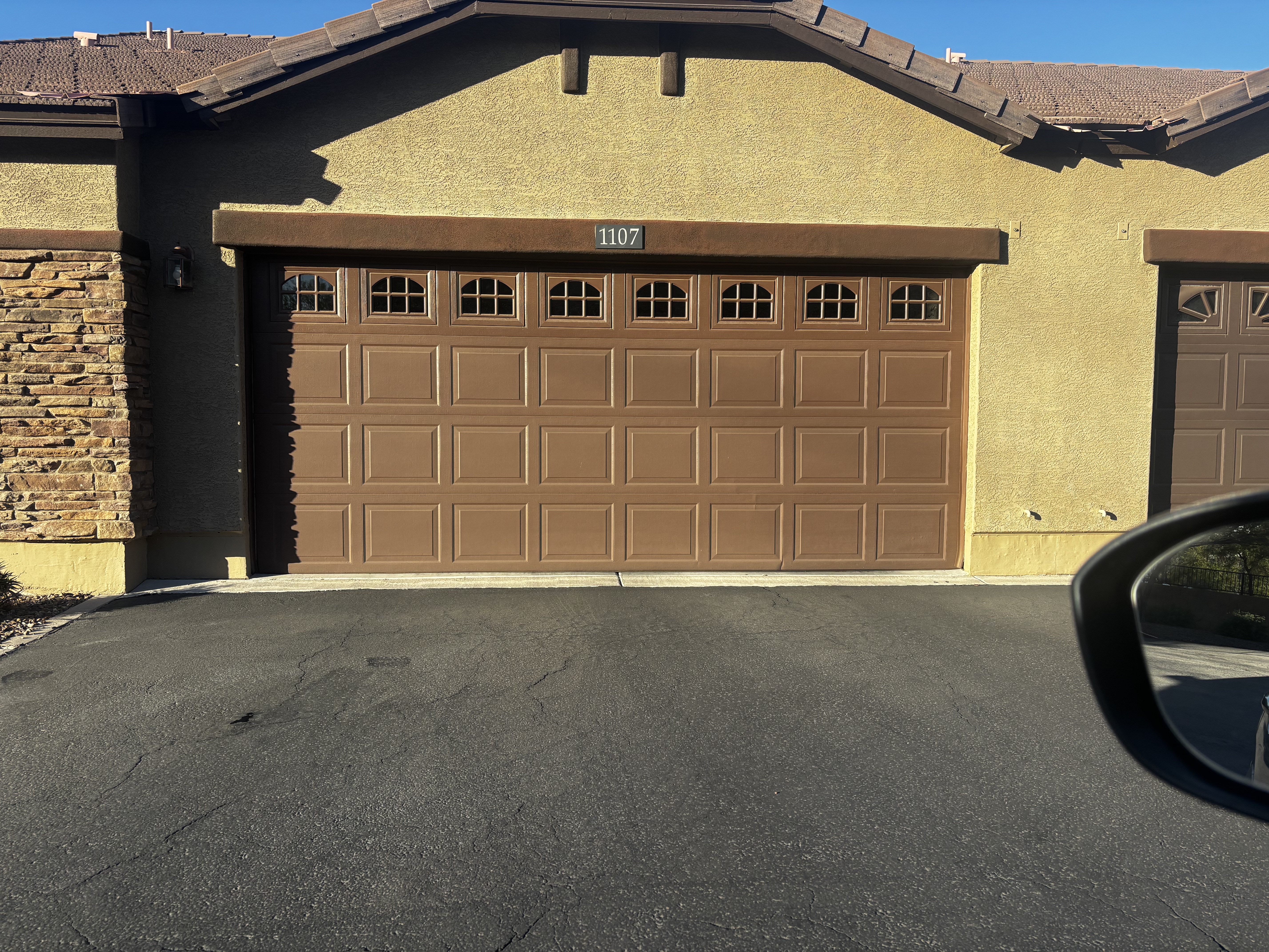 Damaged garage door bottom panel with exposed bracket hardware before repair.