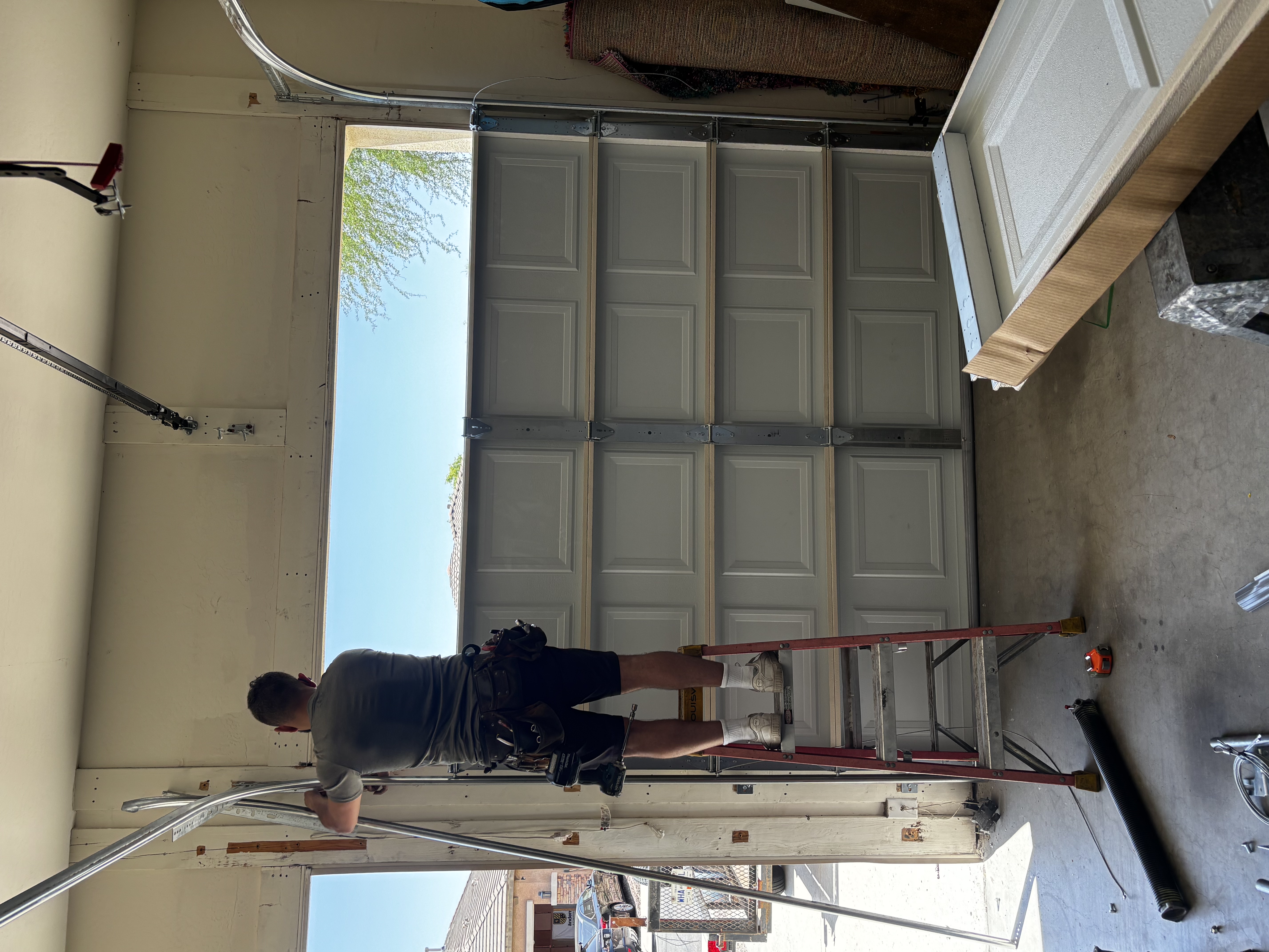 Technician on a ladder fitting new garage door track during an installation.